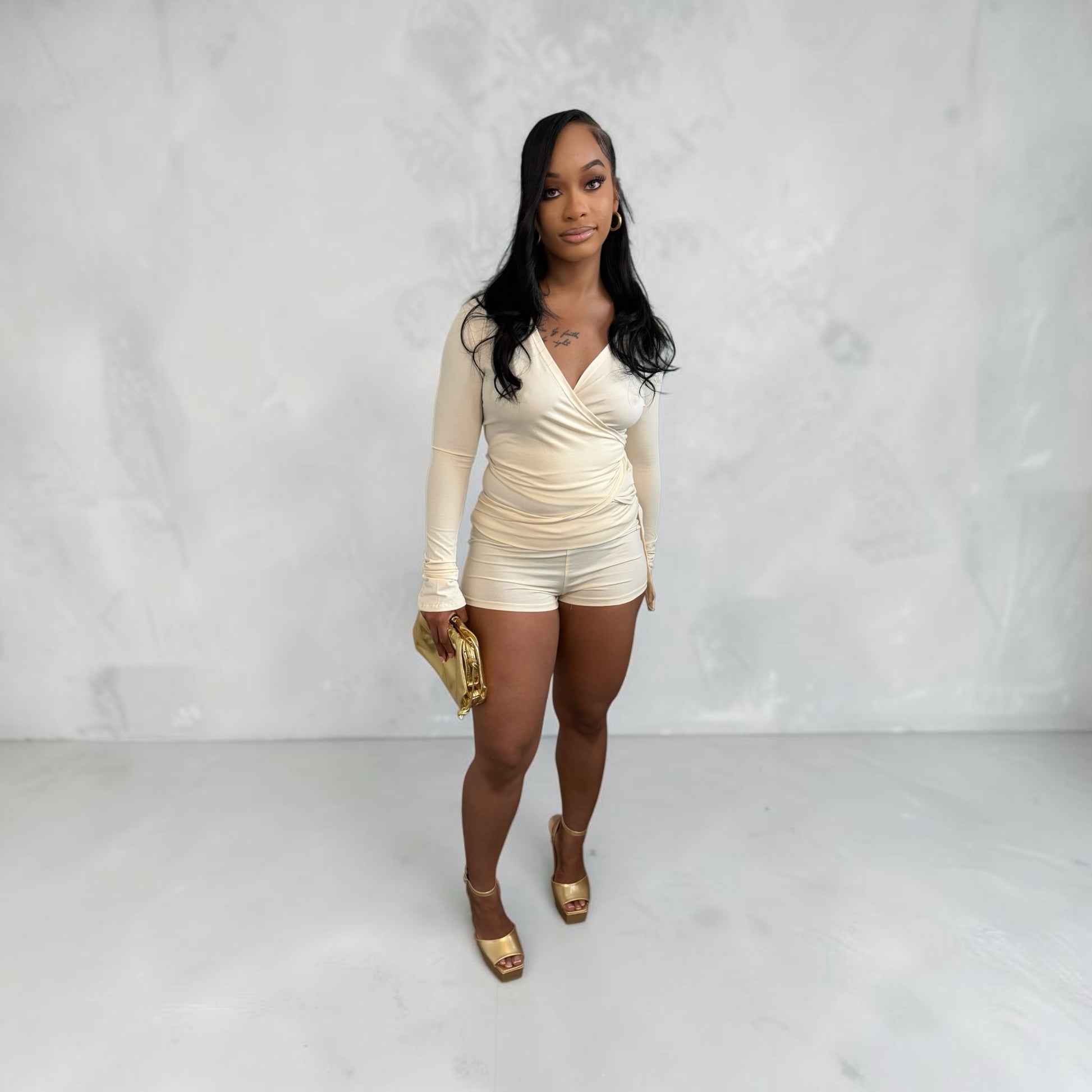 Model wearing 8.Thirteen cream long sleeve wrap top and matching high-waisted shorts with gold heels and clutch.